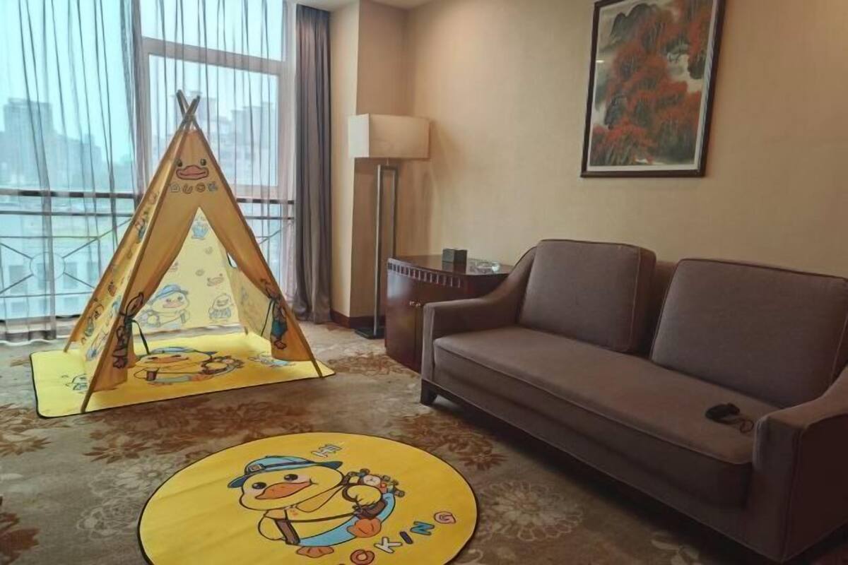 Une pièce avec un canapé marron, un tapis jaune orné de motifs de canards, une structure ressemblant à une tente et un tableau accroché au mur.