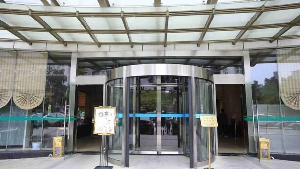 A modern building entrance with a revolving door, glass doors, and a covered entrance area.