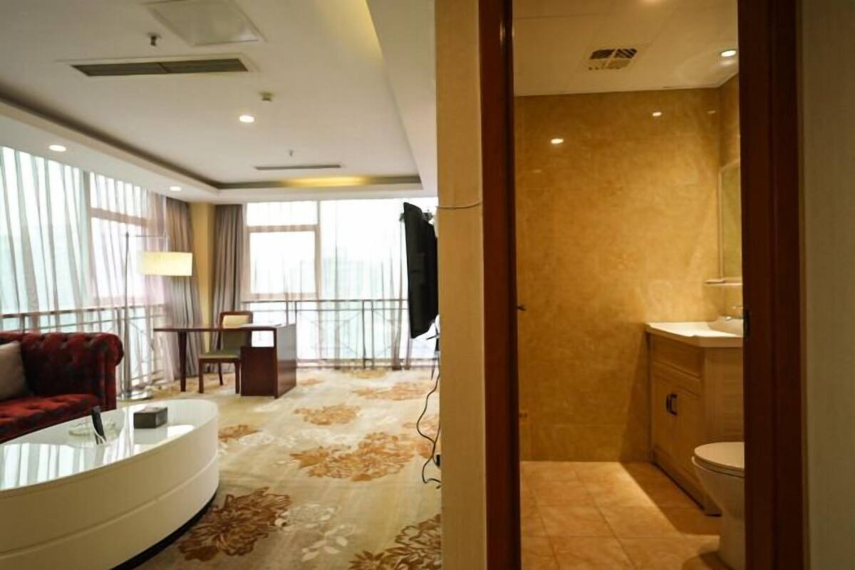 Une chambre d’hôtel dotée d’un espace salon comprenant un canapé, une table basse et une vue sur l’extérieur. La salle de bain est équipée d’une douche, d’un lavabo et de toilettes.