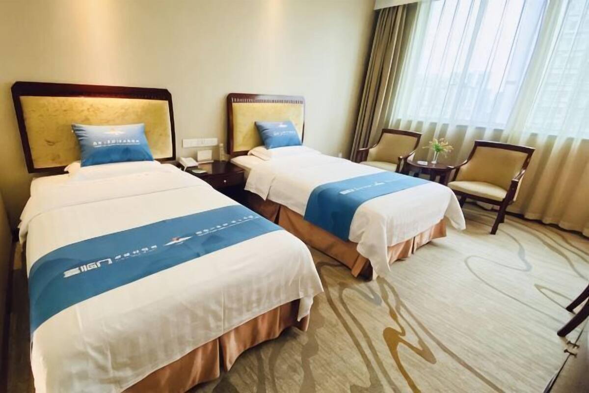 Une chambre d’hôtel avec deux lits, une chaise, une petite table et une fenêtre avec des rideaux.