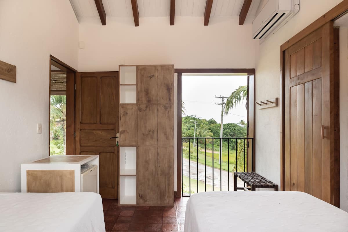 Een kamer met twee bedden, een houten garderobe, een tafeltje en een balkon met uitzicht op groen.