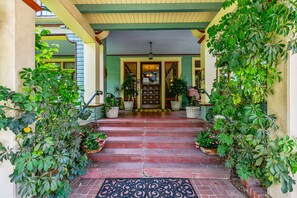 A covered entrance with steps leading to a door, surrounded by potted plants. - The Bissell House Bed and Breakfast (South Pasadena)