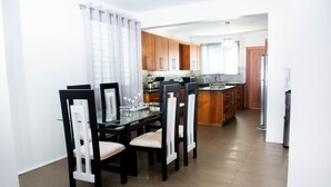 A modern kitchen with wooden cabinets, a dining area with a glass table and chairs, and a stainless steel refrigerator. - Exclusive Penthouse with Hot Tub (Santiago de los Caballeros)