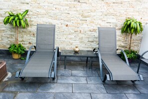 Two lounge chairs with a glass table in front, set against a stone wall with potted plants. - Exclusive Penthouse with Hot Tub (Santiago de los Caballeros)
