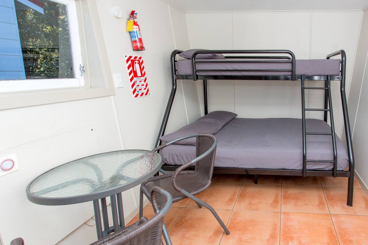 Ein kleines Zimmer mit Etagenbett, einem runden Tisch und Korbstühlen.