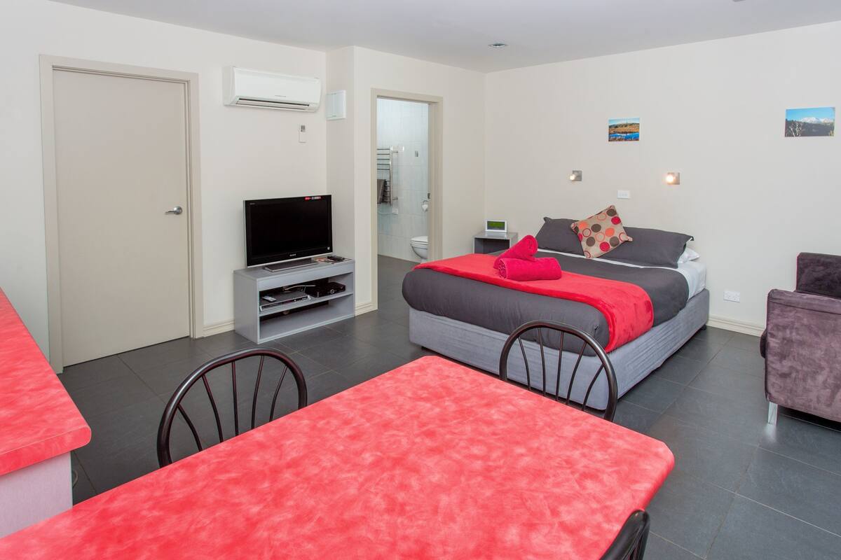 Ein modernes Hotelzimmer mit Bett, Fernseher, Esstisch und Stuhl.