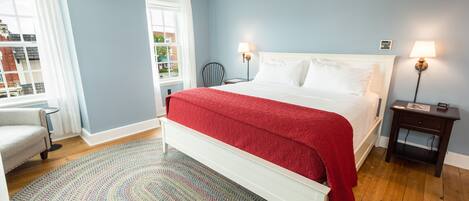 A bedroom with a large bed, a chair, a small table, and a lamp.