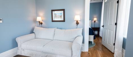 A room with a striped sofa, two wall-mounted lamps, a framed picture, and a wooden floor.
