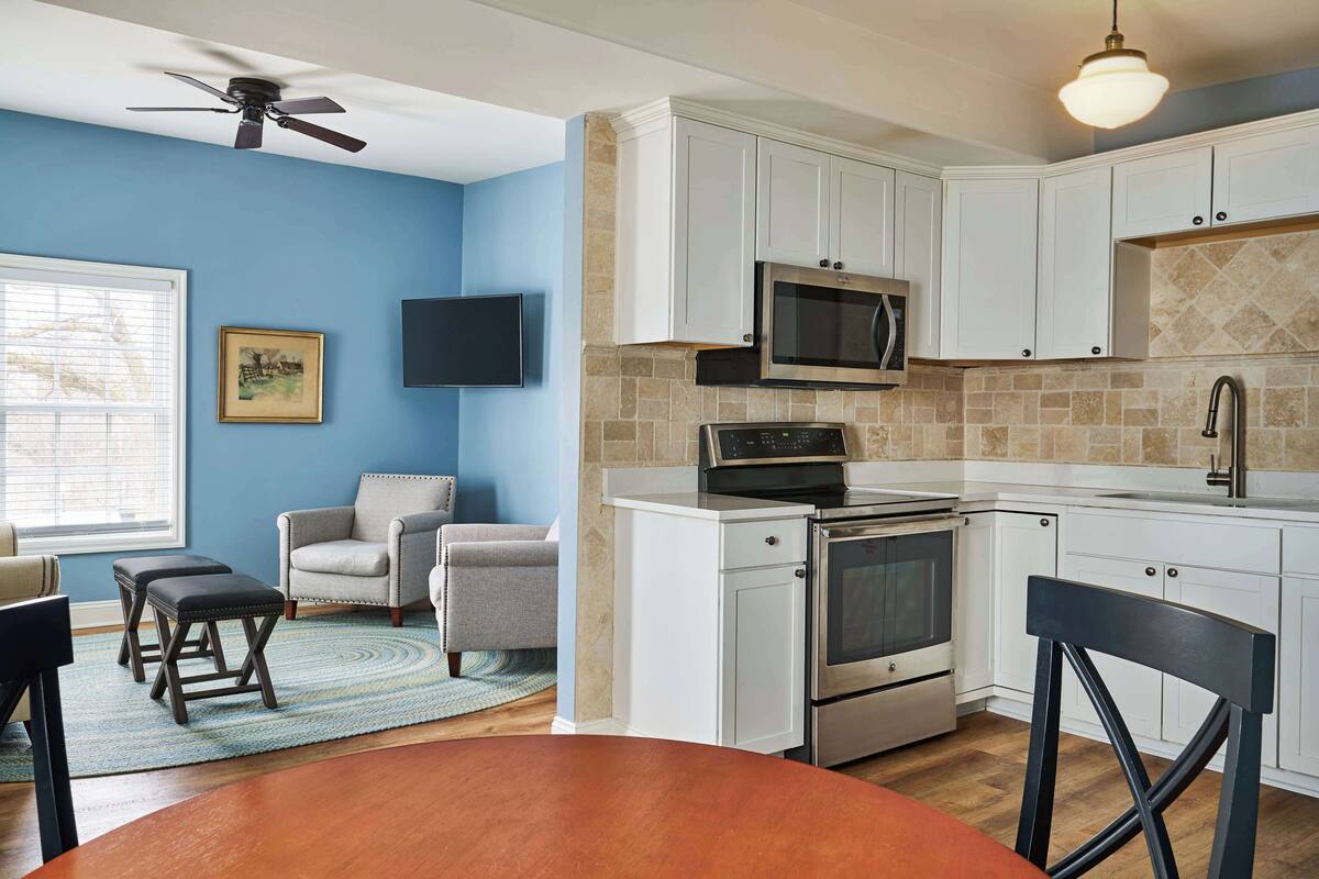 A modern kitchen with white cabinets, a microwave, an oven, and a dining area with a table and chairs.