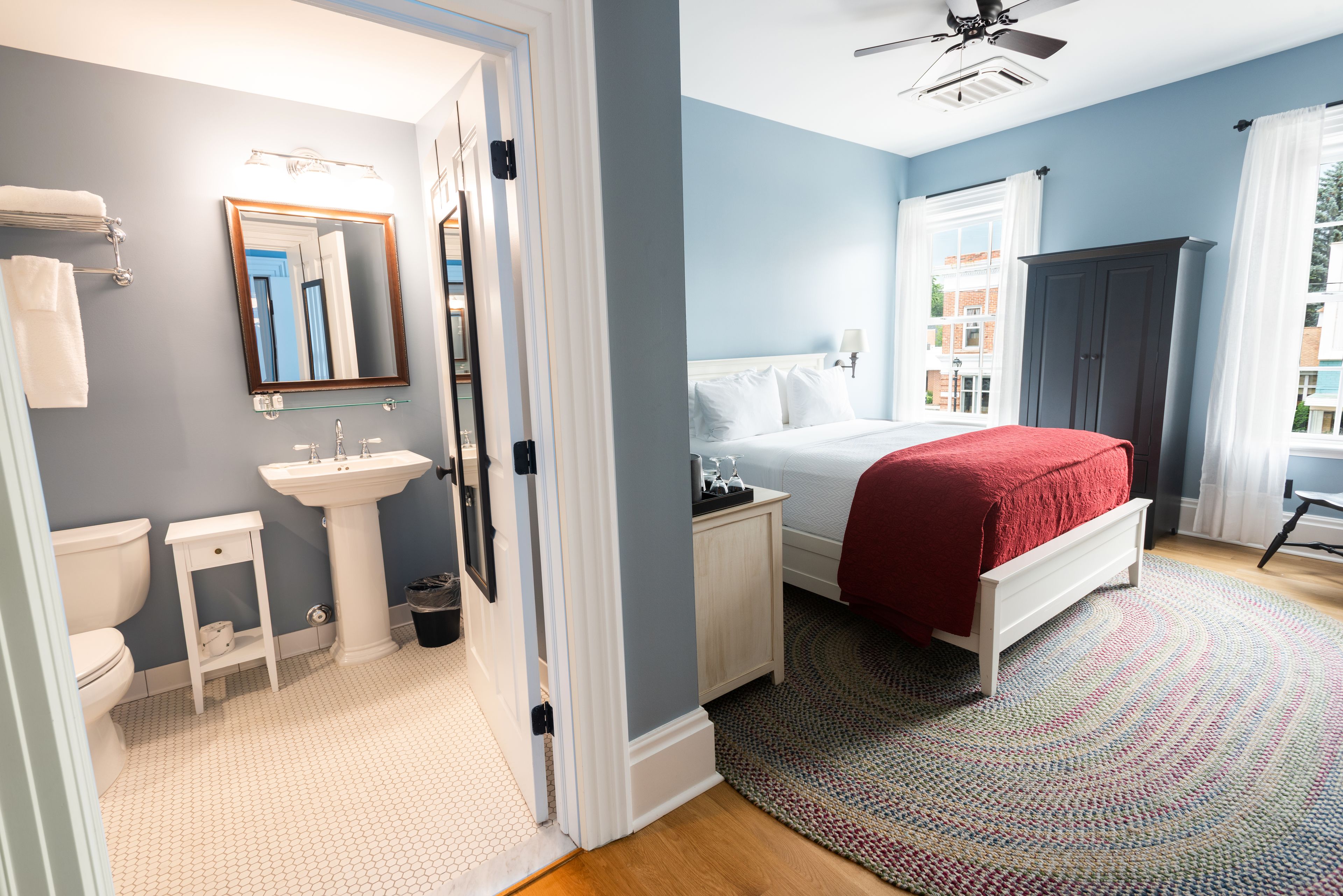 A bedroom with a bed, a nightstand, a dresser, a window with curtains, and a view of buildings outside.