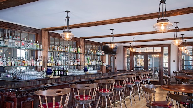 Un espace bar avec des chaises en bois et un comptoir bien garni de bouteilles d’alcool et de verres.