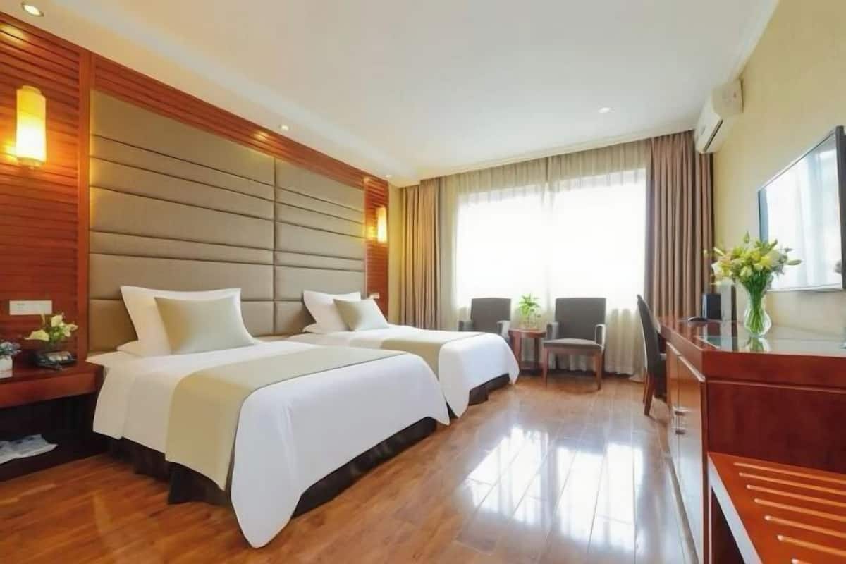 A hotel room with two beds, a desk, a chair, a TV, and a window with curtains.