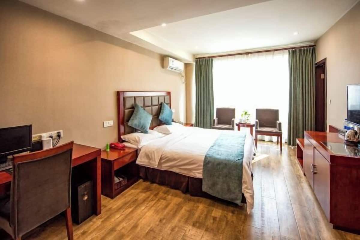 A hotel room with a bed, a desk with a computer, a chair, and a TV.