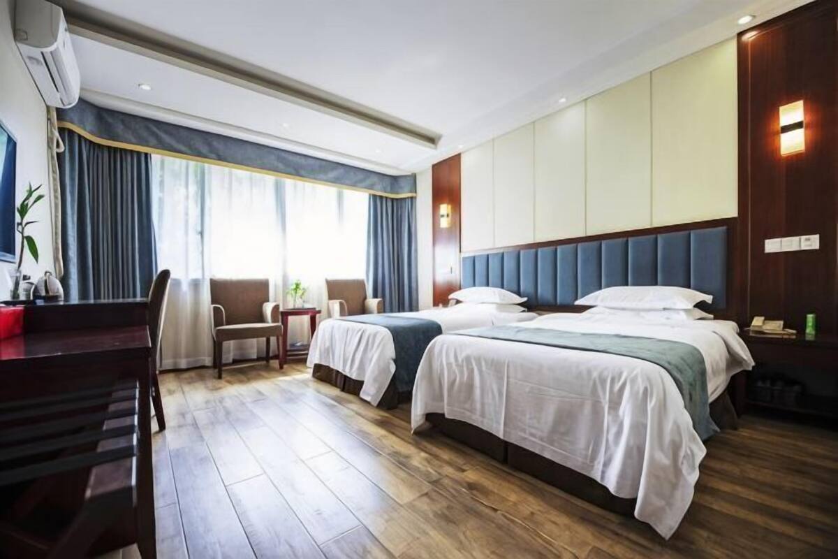 A hotel room with two beds, a desk, a chair, and a large window with curtains.