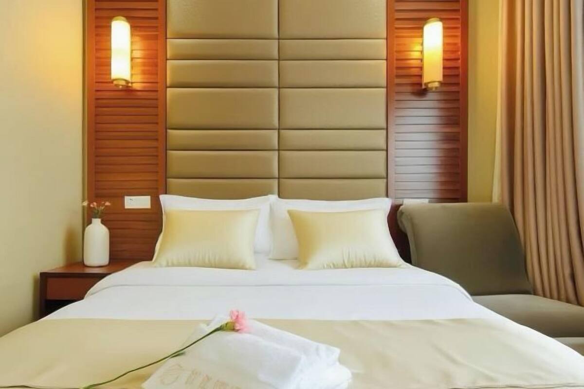 A hotel room with a large bed, two bedside lamps, a nightstand with a vase, and a chair.