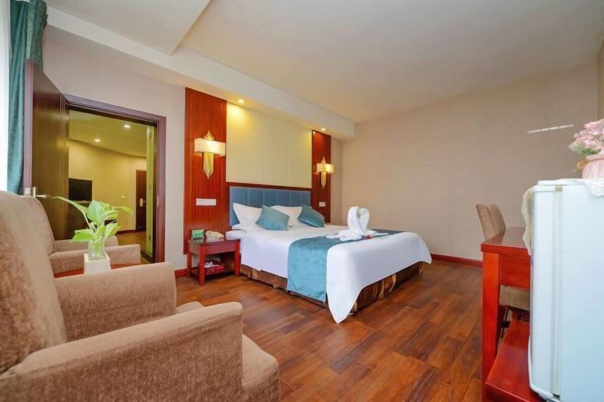 A hotel room with a bed, two bedside tables, a chair, a desk, a plant, and a mirror.