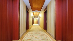 Passadís d'hotel amb una catifes estampada, portes de fusta i un lluminari al sostre.
