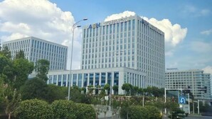 Un hotel modern amb un cartell ben visible de 'Novotel', envoltat de vegetació exuberant i altres edificis.