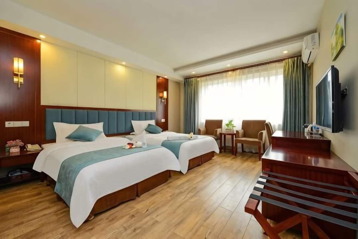 A hotel room with two beds, a desk, a chair, a TV, and a window with curtains.