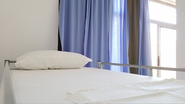 A single bed with white bedding, a white pillow, and a metal frame. There are blue curtains on the window behind the bed. - Hostel Hasta La Vista (Sarandë)