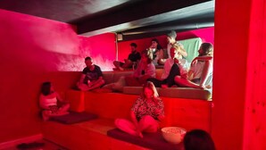 A group of people sitting on a red-colored sofa in a room with a low ceiling and a visible duct.