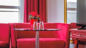 A red sofa, a small round table with a potted plant, two glasses, and a television on a wooden stand.