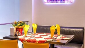 A dining area with a checkered tablecloth, yellow napkins, and a cityscape painting on the wall.