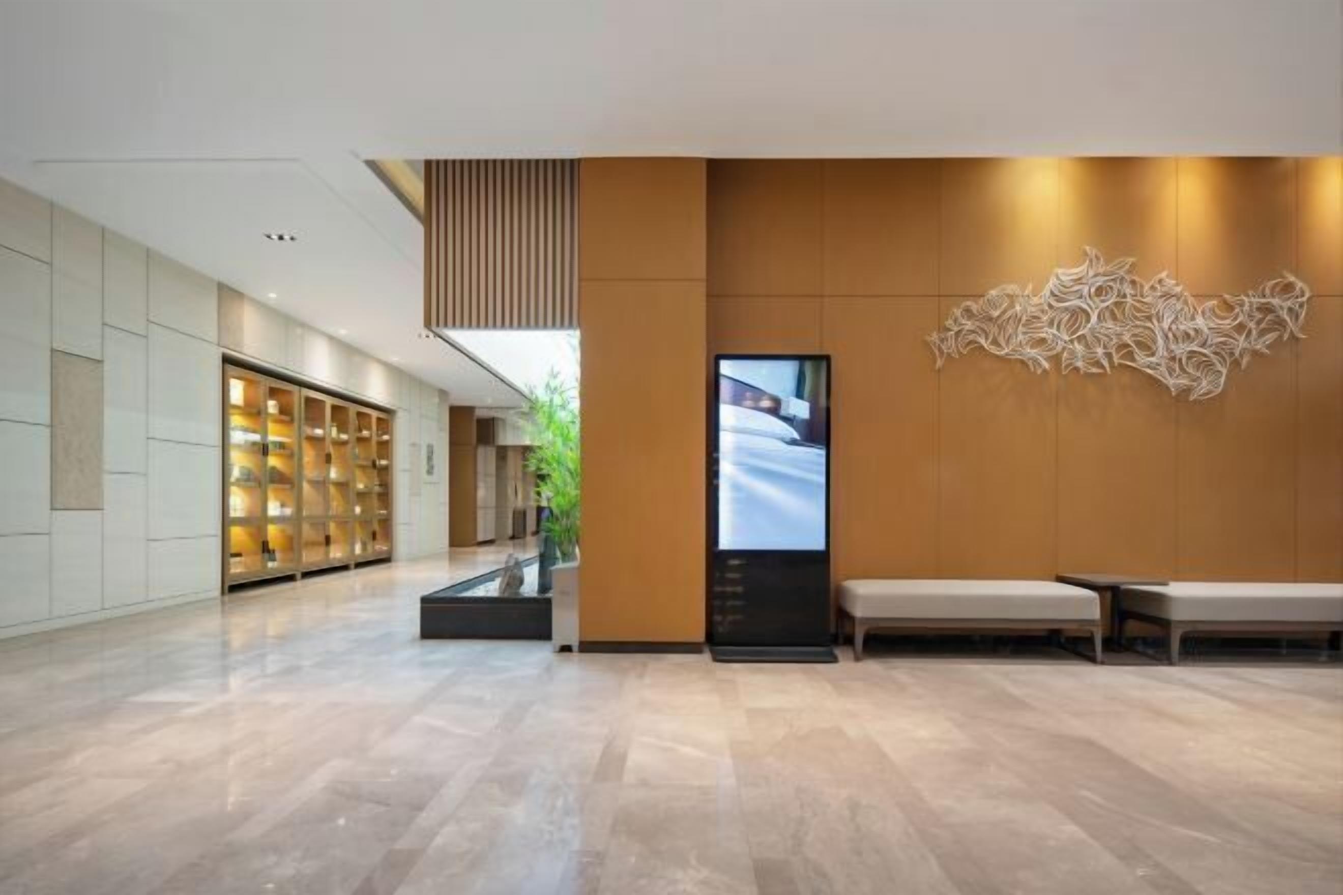 A modern hotel lobby with a reception desk, seating area, and a large digital display.