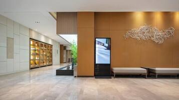 A modern hotel lobby with a reception desk, seating area, and a large digital display.