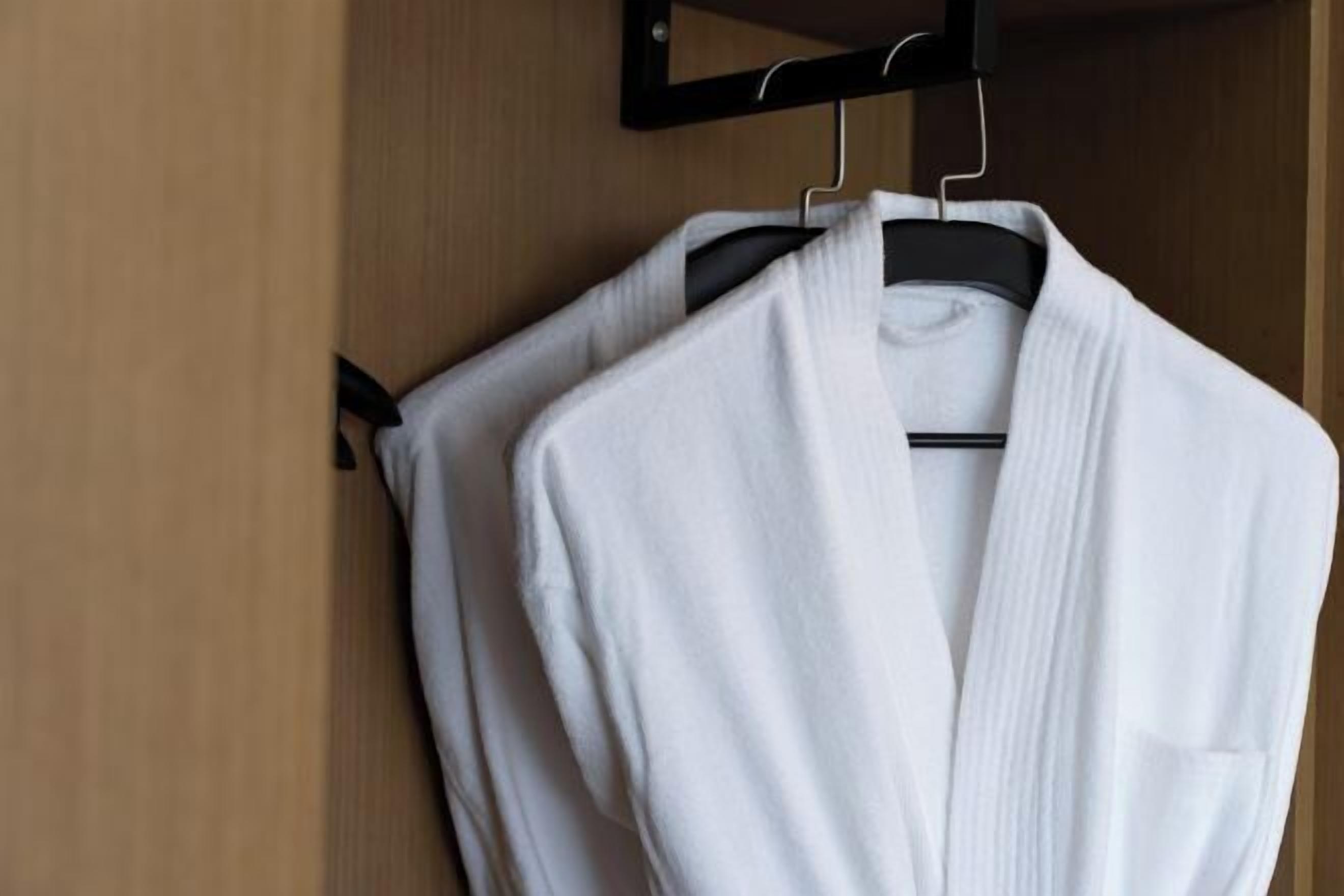 A white robe hanging on a black hanger in a wooden closet.
