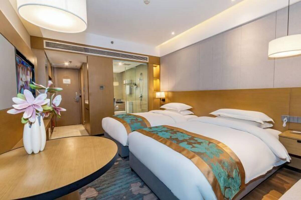 A hotel room with a large bed, bedside tables, a round table with a vase of flowers, and a mirror.