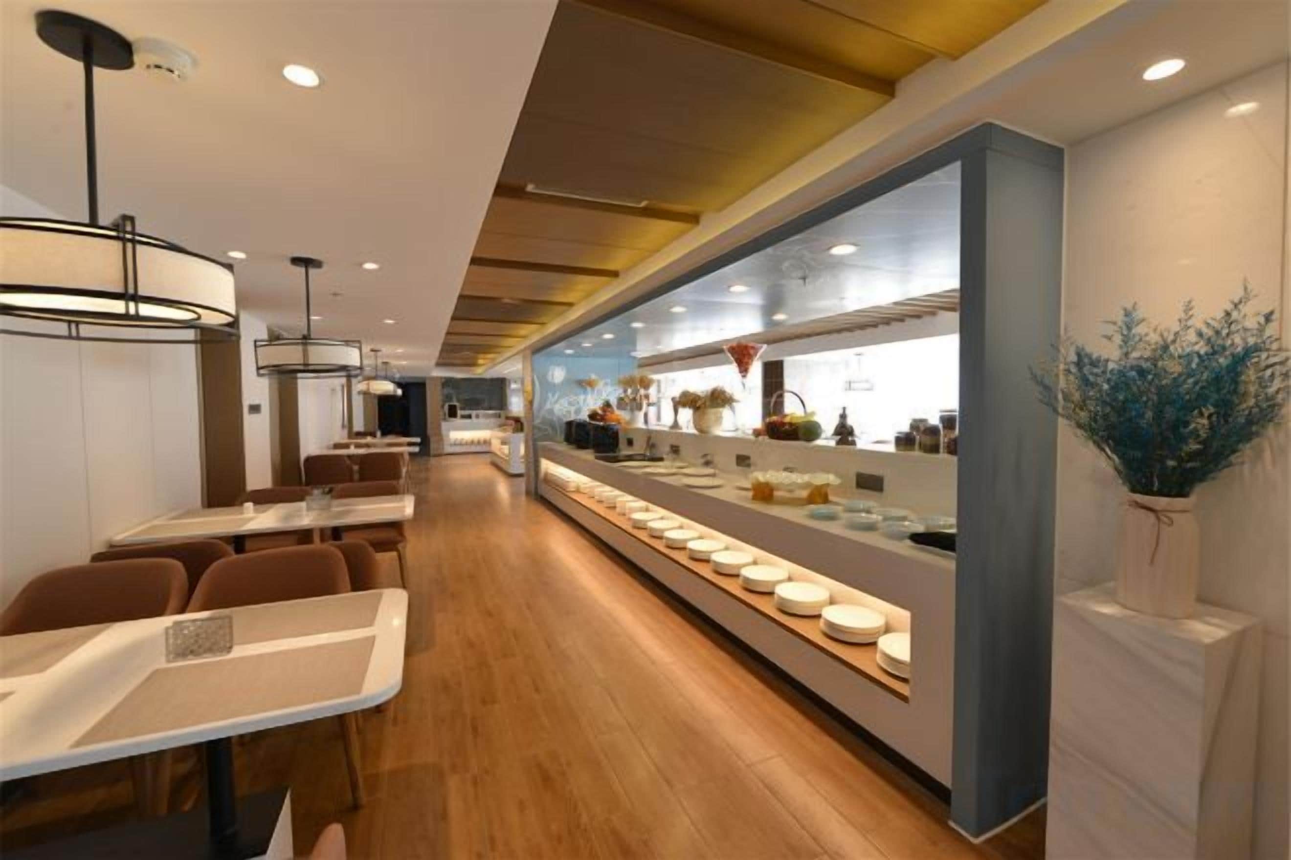 Een modern restaurantinterieur met lange tafels, een toonbank met etalage en een keuken op de achtergrond.