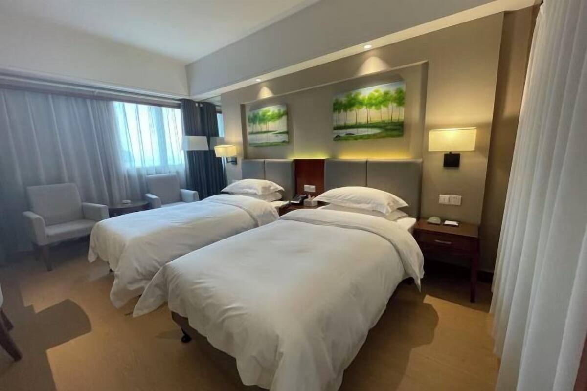 A hotel room with two beds, a desk, a chair, and two wall-mounted lamps.