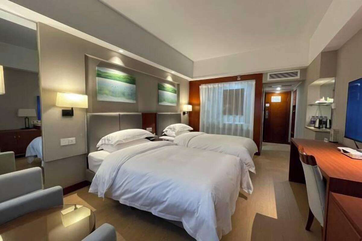 A hotel room with two beds, a desk, a chair, and a television.