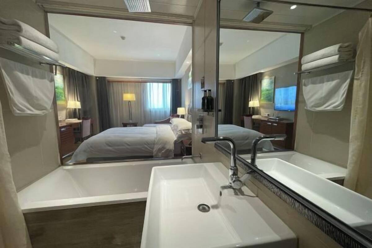 A hotel room with a large mirror, a bathtub, a sink, and a bed.