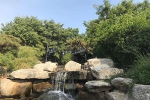 A waterfall cascading over large rocks with a small structure in the background. - Hongbao Hotel (Xuchang Caowei Ancient City Pang Donglai Times Square) (Xuchang)