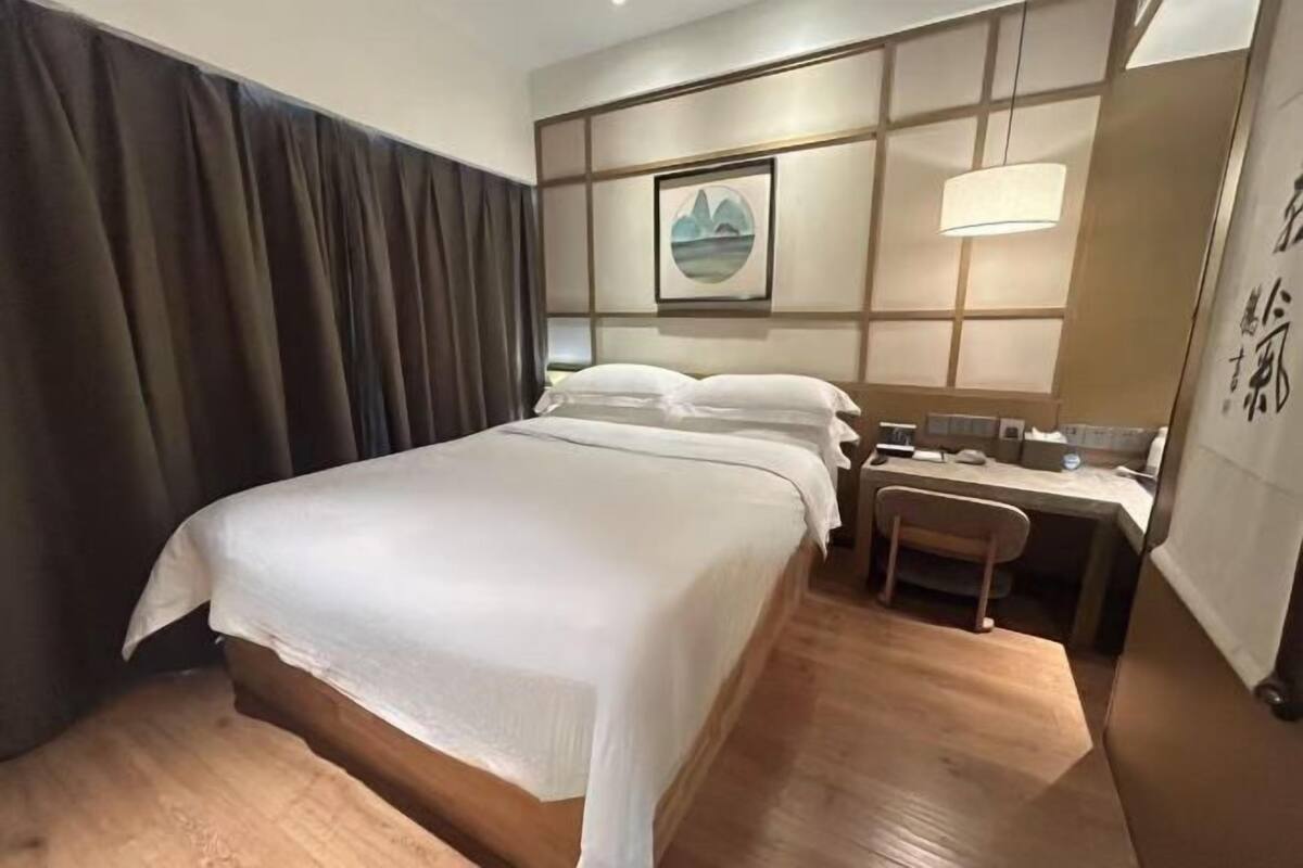 A hotel room with a bed, desk, chair, and artwork on the wall.