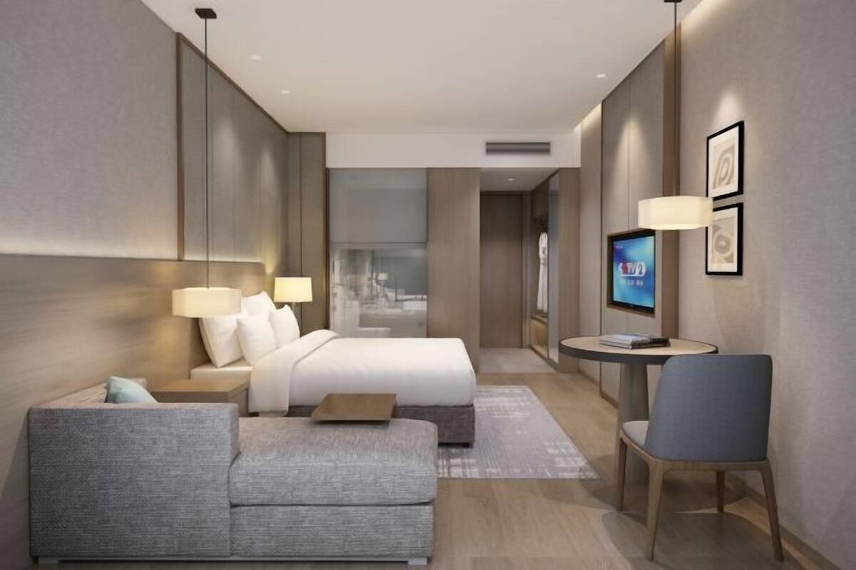 A modern hotel room with a bed, a sofa, a TV, and a desk.