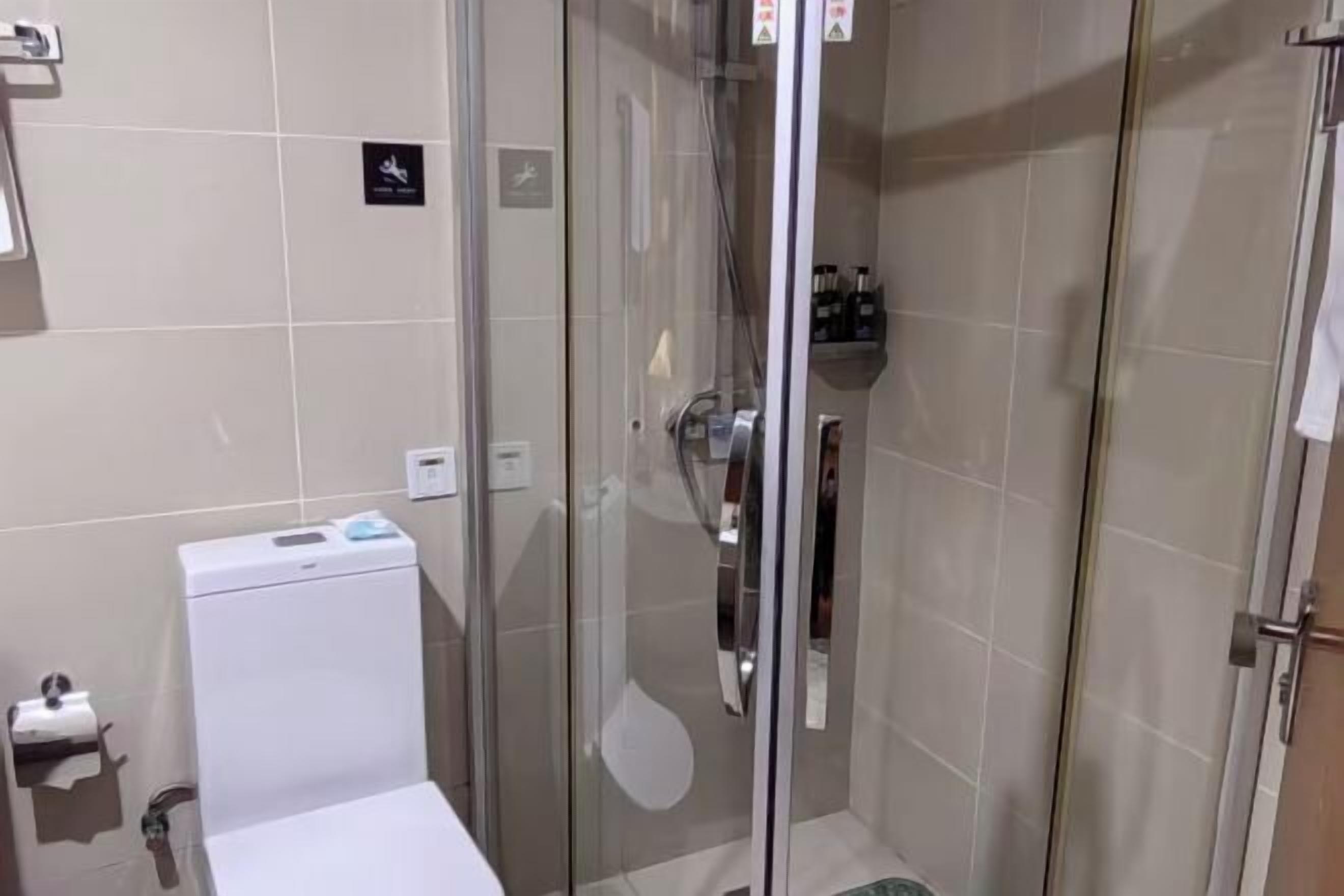 Un baño con inodoro, cabina de ducha de vidrio y repisa con artículos de aseo.