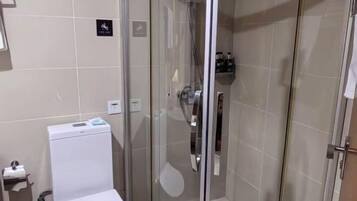 Un baño con inodoro, cabina de ducha de vidrio y repisa con artículos de aseo.