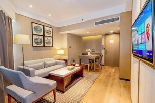 Una habitación de hotel moderna con sofá, sillones, una mesa de centro, televisor y zona de comedor.