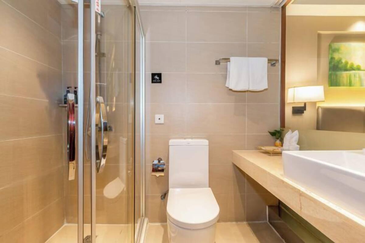 A modern bathroom with a glass shower enclosure, a white toilet, and a beige-tiled sink area.