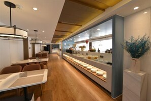 A modern restaurant with long tables, a central counter with food displays, and a wooden floor. - Hongbao Hotel (Xuchang Caowei Ancient City Pang Donglai Times Square) (Xuchang)