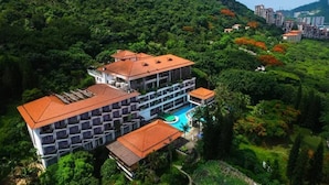 Um hotel com vários andares, piscina e vegetação exuberante, cercado por colinas.