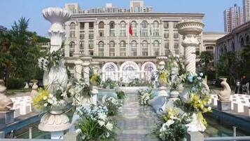 A grand hotel facade with a central fountain, surrounded by ornate columns and floral arrangements.
