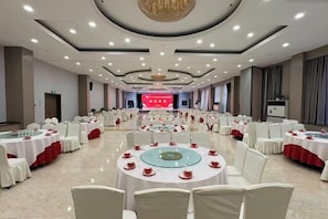 A banquet hall with round tables, chairs, and a stage at the front. - Fengleyuan Hotel (Zhengzhou)