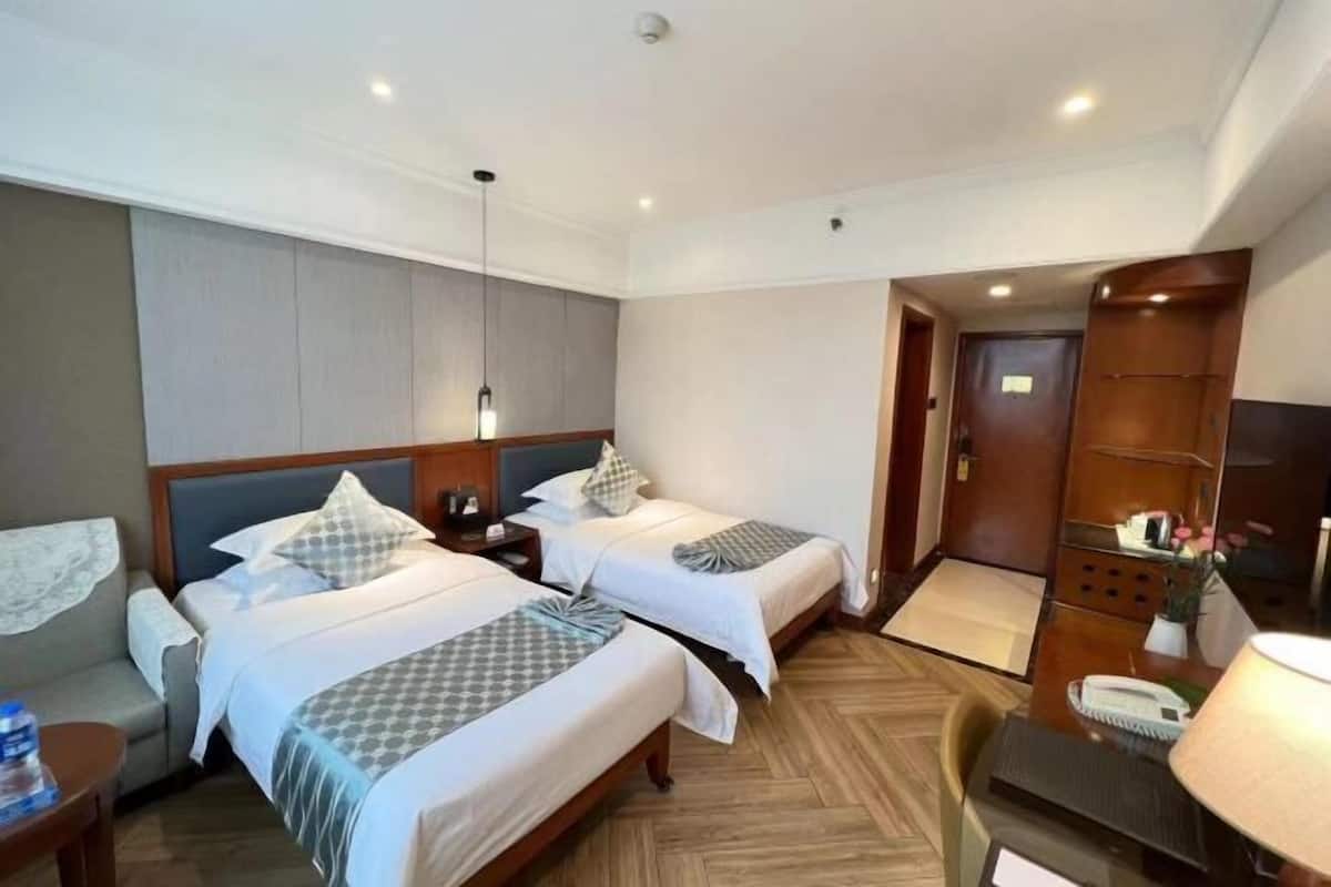 A hotel room with two beds, a desk, a chair, a lamp, and a wardrobe.