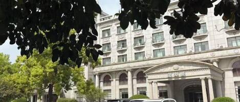 A hotel with a classical facade, a parking lot with several cars, and a well-maintained lawn.