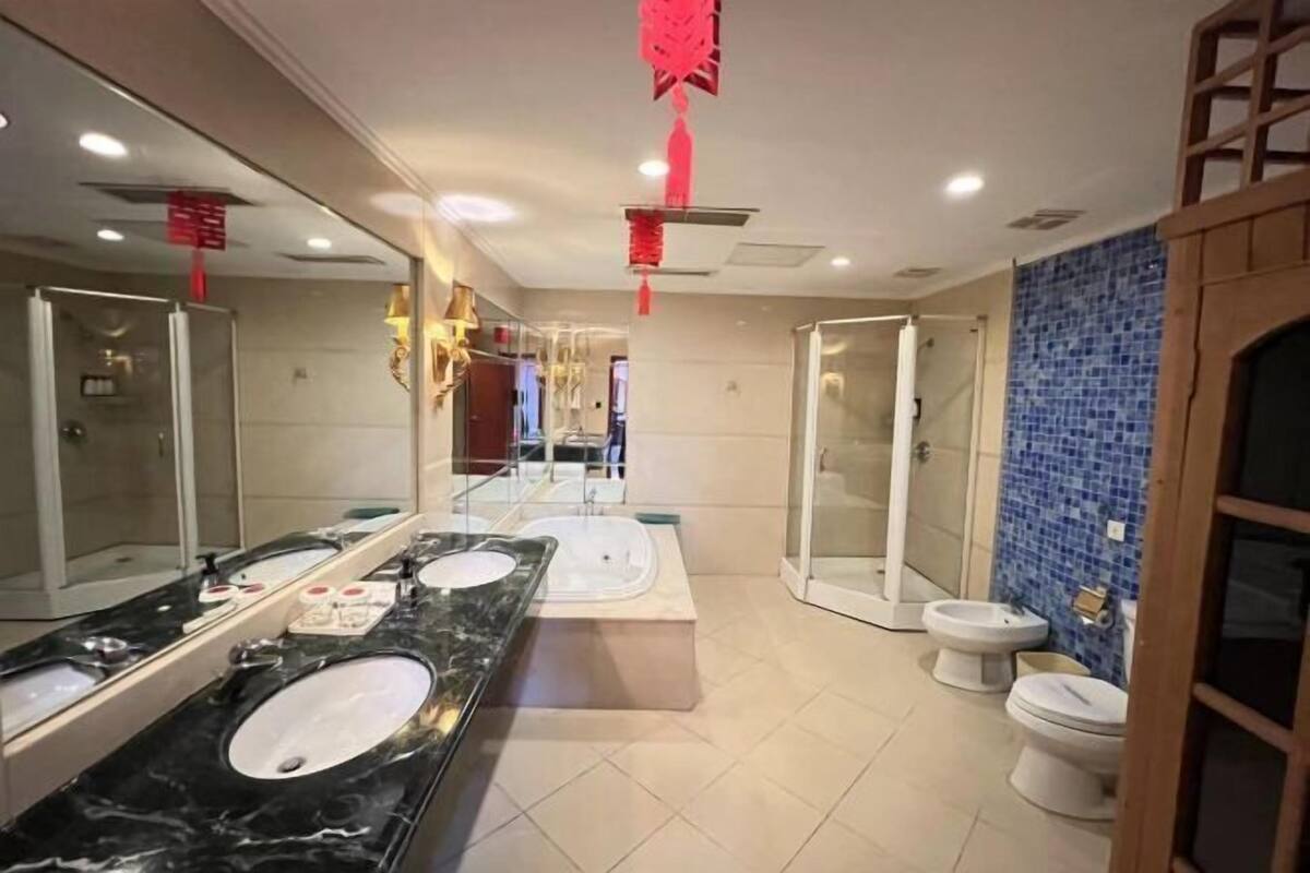 A modern bathroom with a large mirror, multiple sinks, a shower area, and a toilet.