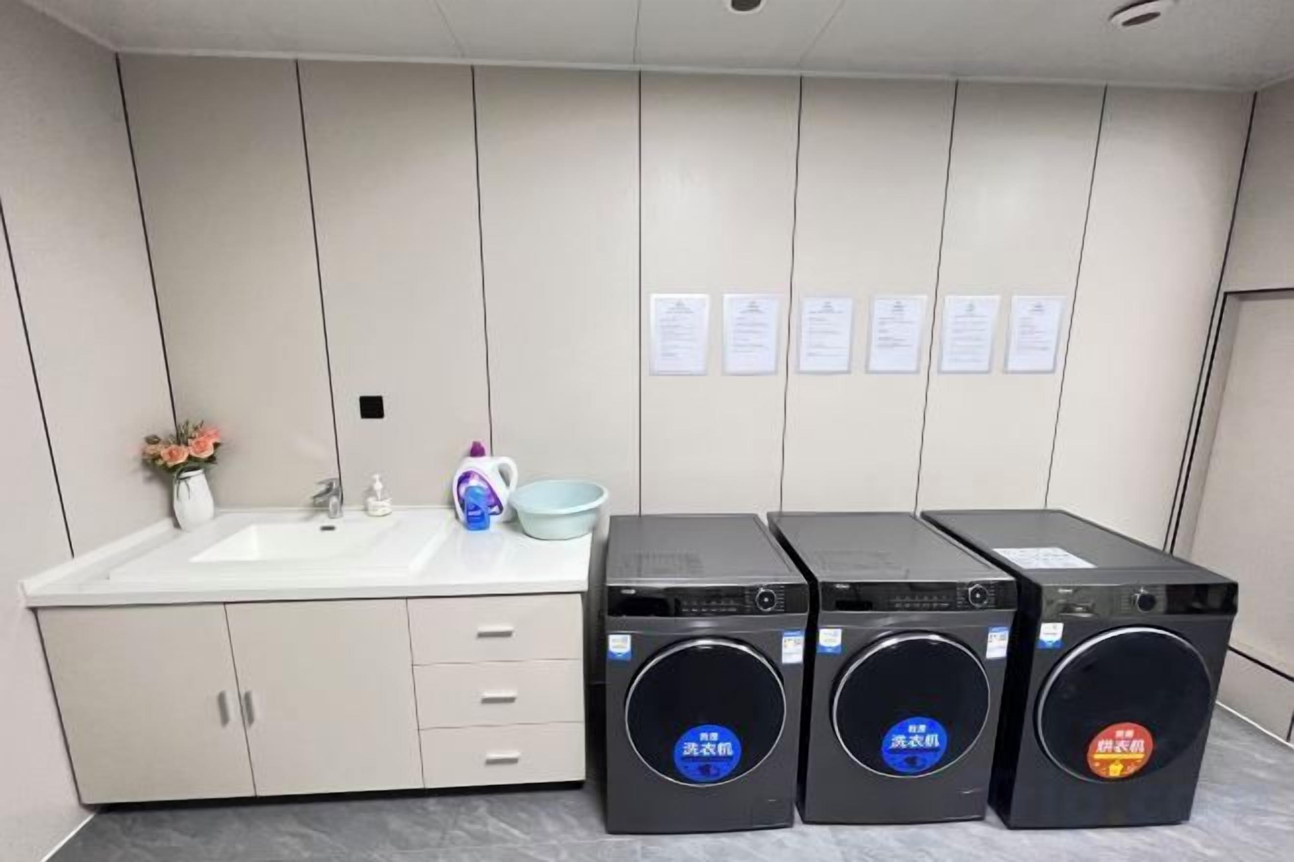 A hotel bathroom with a sink, mirror, and three black washing machines.